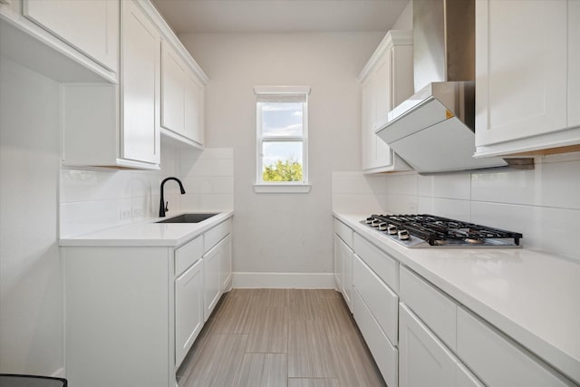 kitchen featuring sink, white cabinetry, backsplash, stainless steel gas stovetop, and wall chimney exhaust hood