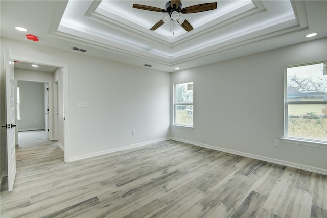 empty room featuring crown molding, a tray ceiling, light hardwood / wood-style floors, and ceiling fan