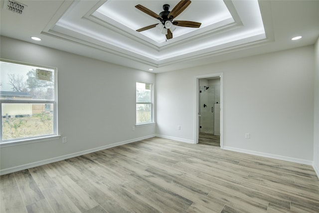 spare room with ceiling fan, light wood-type flooring, and a tray ceiling