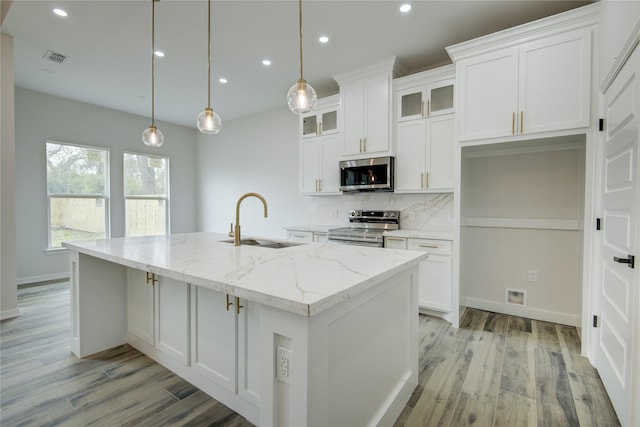 kitchen with sink, light stone counters, decorative light fixtures, stainless steel appliances, and a kitchen island with sink