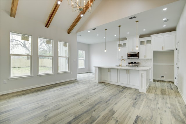 kitchen with appliances with stainless steel finishes, pendant lighting, white cabinets, a kitchen island with sink, and light wood-type flooring