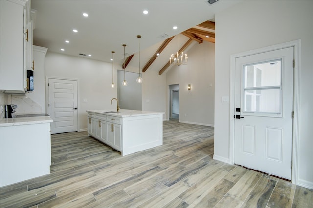 kitchen with decorative light fixtures, white cabinetry, an island with sink, sink, and stove