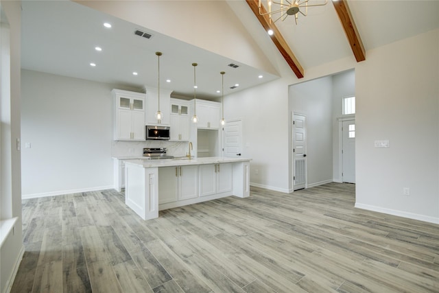 kitchen with high vaulted ceiling, hanging light fixtures, appliances with stainless steel finishes, a kitchen island with sink, and white cabinets