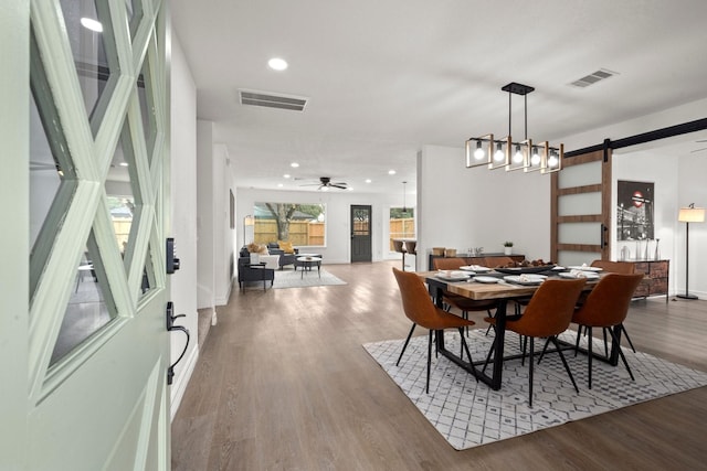 dining space with wood-type flooring, a barn door, and ceiling fan