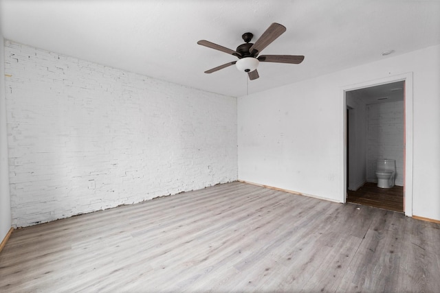 spare room with brick wall, ceiling fan, and light hardwood / wood-style flooring