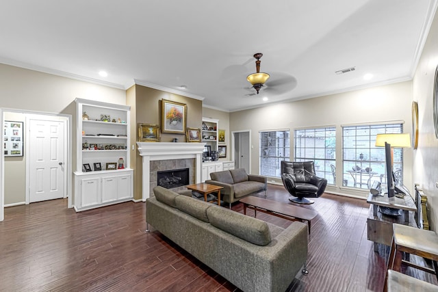 living room featuring a tiled fireplace, ceiling fan, crown molding, and dark hardwood / wood-style flooring