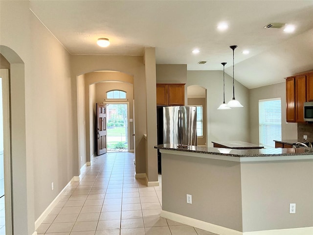 kitchen featuring lofted ceiling, decorative light fixtures, light tile patterned floors, dark stone countertops, and stainless steel appliances