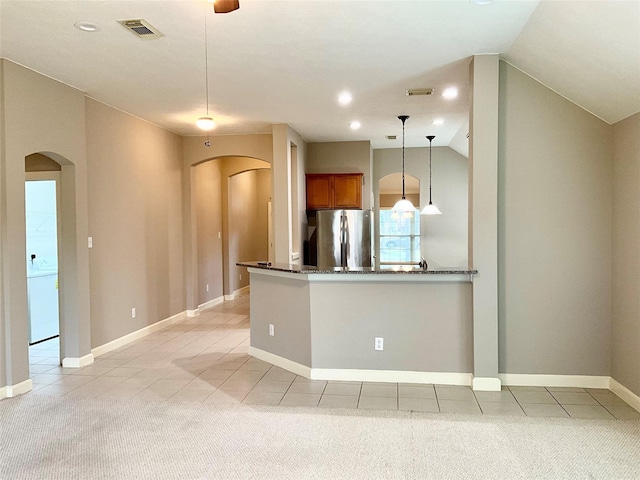 kitchen featuring pendant lighting, lofted ceiling, stainless steel refrigerator, dark stone countertops, and kitchen peninsula