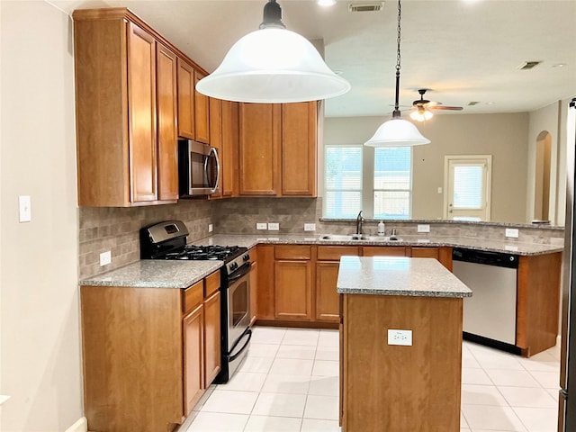 kitchen with a kitchen island, light stone countertops, appliances with stainless steel finishes, and pendant lighting