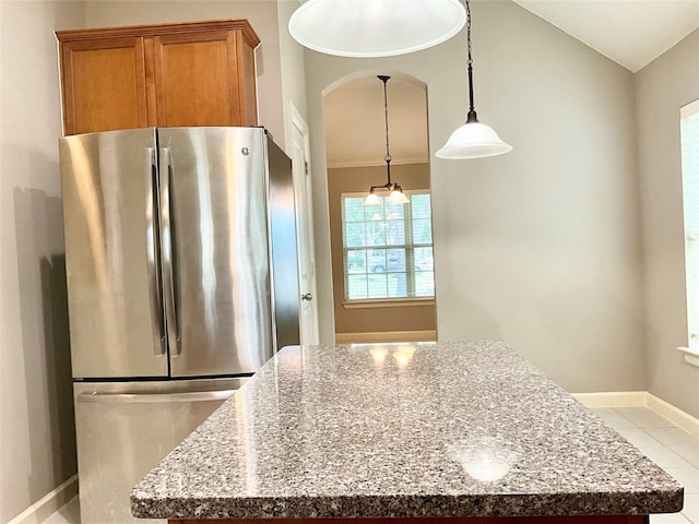 kitchen featuring light stone counters, hanging light fixtures, light tile patterned floors, and stainless steel fridge