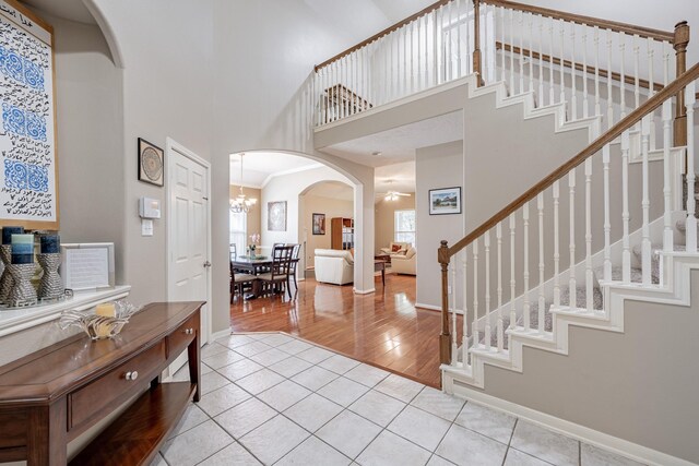 tiled entryway with an inviting chandelier, ornamental molding, and a high ceiling