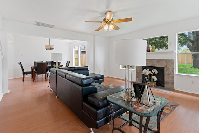 living room with a premium fireplace, ceiling fan, and light wood-type flooring