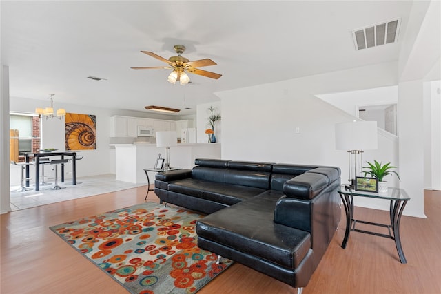 living room with ceiling fan with notable chandelier and light hardwood / wood-style flooring