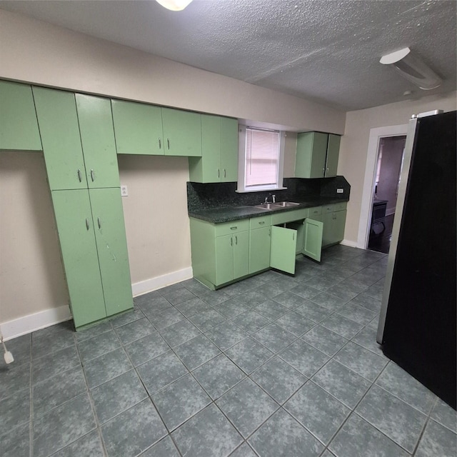 kitchen with sink, green cabinets, a textured ceiling, and stainless steel refrigerator