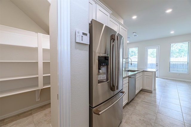 kitchen featuring sink, appliances with stainless steel finishes, white cabinetry, light stone countertops, and a healthy amount of sunlight