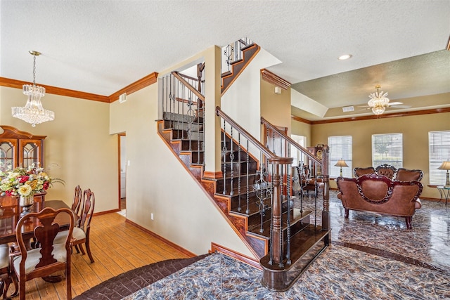 stairway featuring hardwood / wood-style flooring, ornamental molding, a textured ceiling, ceiling fan with notable chandelier, and a raised ceiling