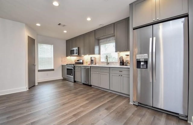 kitchen with sink, light hardwood / wood-style flooring, gray cabinets, appliances with stainless steel finishes, and decorative backsplash