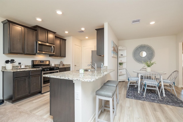 kitchen featuring appliances with stainless steel finishes, light hardwood / wood-style flooring, light stone counters, and kitchen peninsula