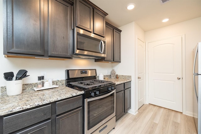 kitchen featuring light stone counters, dark brown cabinets, stainless steel appliances, and light hardwood / wood-style floors