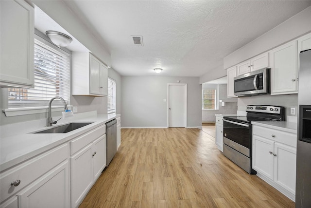 kitchen with appliances with stainless steel finishes, sink, white cabinets, and light hardwood / wood-style floors