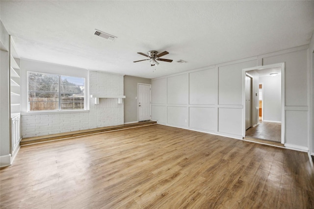 unfurnished bedroom featuring ceiling fan, hardwood / wood-style flooring, a textured ceiling, and brick wall