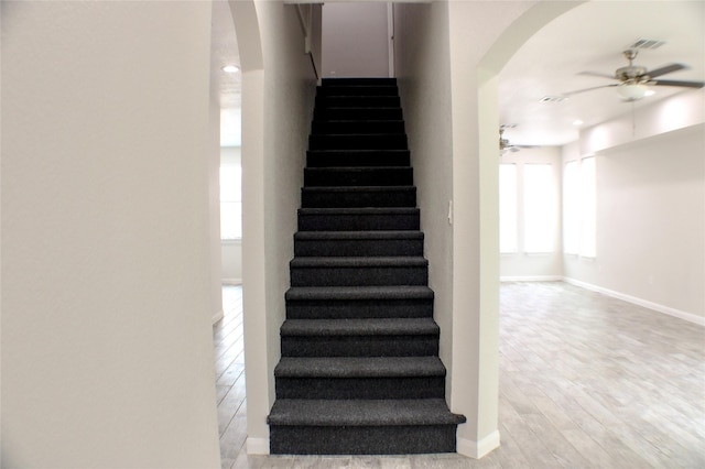 staircase with wood-type flooring and ceiling fan