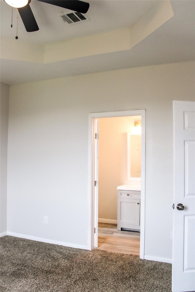 unfurnished room with ceiling fan, a raised ceiling, and light carpet