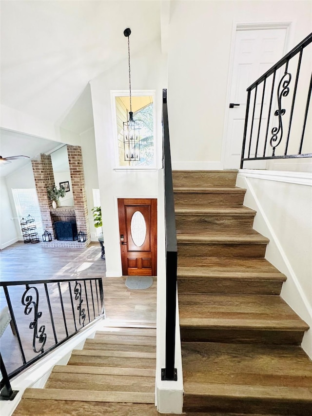 stairs featuring wood-type flooring, a chandelier, high vaulted ceiling, and a brick fireplace