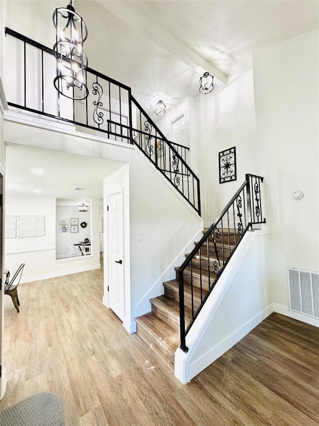 stairs with beam ceiling, a notable chandelier, hardwood / wood-style flooring, and high vaulted ceiling