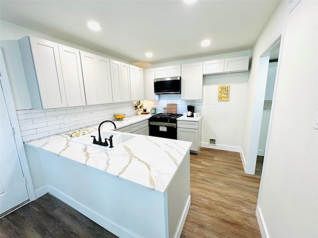 kitchen with black range with gas cooktop, light stone counters, a peninsula, a sink, and stainless steel microwave