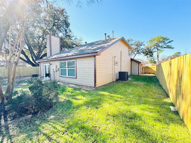 view of side of home featuring a fenced backyard, a yard, a chimney, and central AC unit