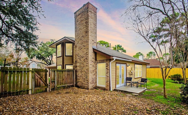 back of property at dusk featuring a patio, a fenced backyard, brick siding, a yard, and a chimney