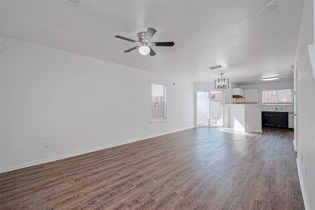 unfurnished living room with sink, dark wood-type flooring, ceiling fan with notable chandelier, and a textured ceiling