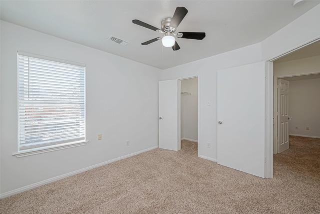 unfurnished bedroom featuring ceiling fan, light colored carpet, a closet, and a walk in closet