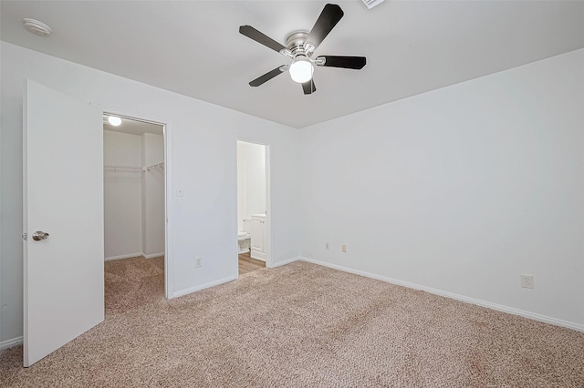 unfurnished bedroom featuring a spacious closet, light colored carpet, ceiling fan, ensuite bath, and a closet