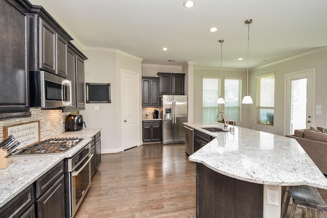 kitchen featuring sink, hanging light fixtures, ornamental molding, an island with sink, and stainless steel appliances