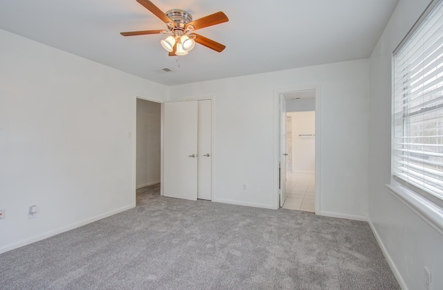 unfurnished bedroom with multiple windows, ceiling fan, light colored carpet, and ensuite bath