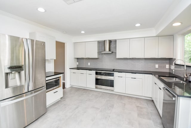 kitchen featuring wall chimney range hood, sink, appliances with stainless steel finishes, white cabinetry, and decorative backsplash