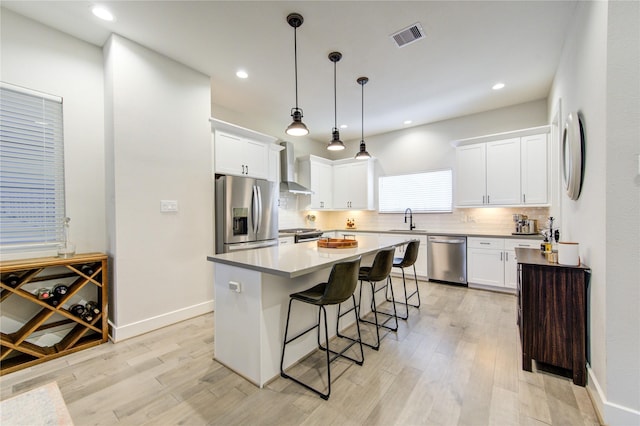 kitchen featuring a kitchen island, sink, white cabinets, stainless steel appliances, and wall chimney range hood