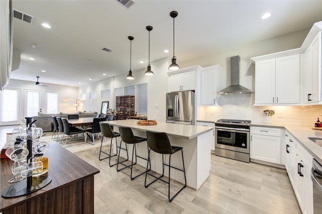 kitchen with white cabinetry, stainless steel appliances, a center island, and wall chimney range hood