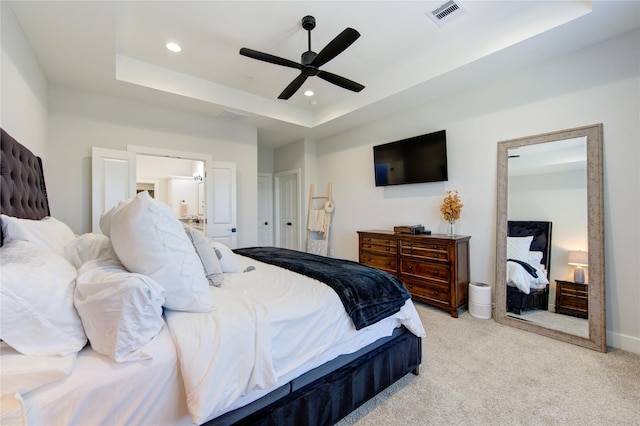 carpeted bedroom with a raised ceiling, connected bathroom, and ceiling fan