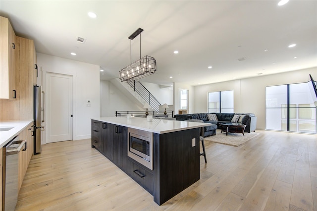 kitchen featuring stainless steel appliances, a kitchen breakfast bar, light hardwood / wood-style floors, a center island with sink, and decorative light fixtures