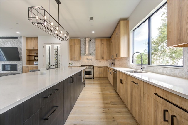 kitchen with wall chimney exhaust hood, sink, decorative light fixtures, appliances with stainless steel finishes, and backsplash