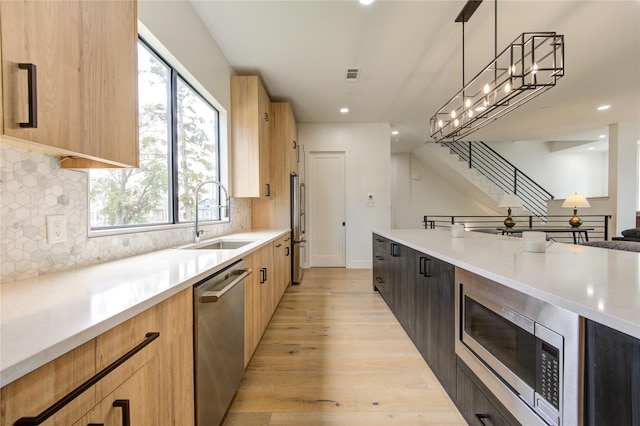 kitchen featuring sink, appliances with stainless steel finishes, hanging light fixtures, tasteful backsplash, and light hardwood / wood-style floors