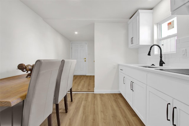 kitchen with tasteful backsplash, sink, white cabinets, and light hardwood / wood-style flooring