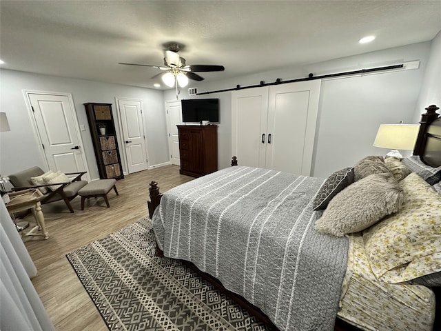 bedroom featuring hardwood / wood-style flooring, a barn door, and ceiling fan