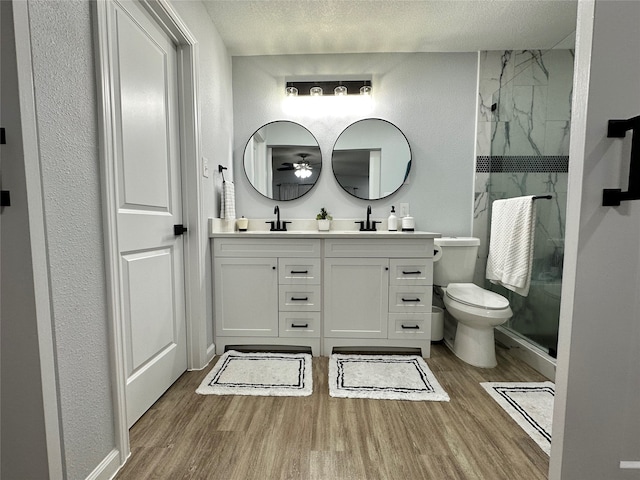 bathroom with a tile shower, wood-type flooring, vanity, toilet, and a textured ceiling