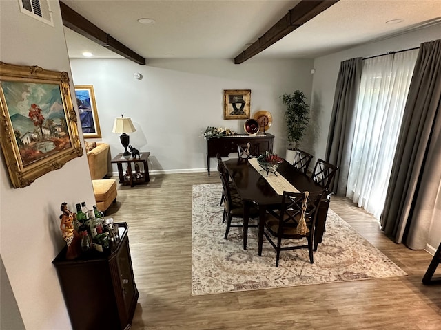 dining space with light hardwood / wood-style flooring and beamed ceiling