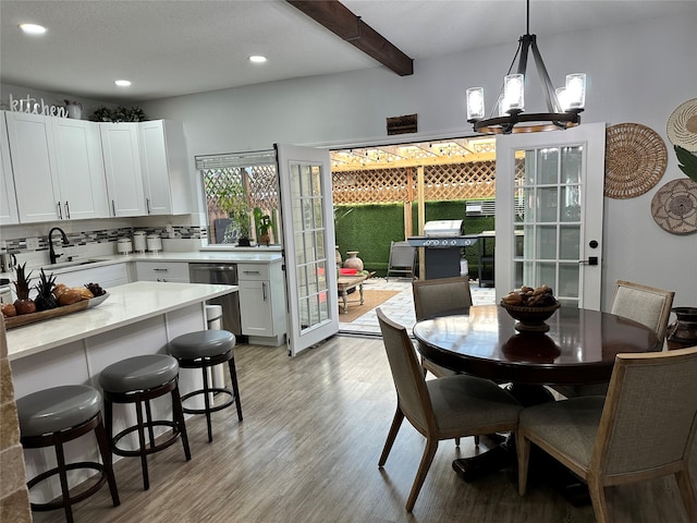 dining space featuring an inviting chandelier, sink, light hardwood / wood-style flooring, beam ceiling, and french doors