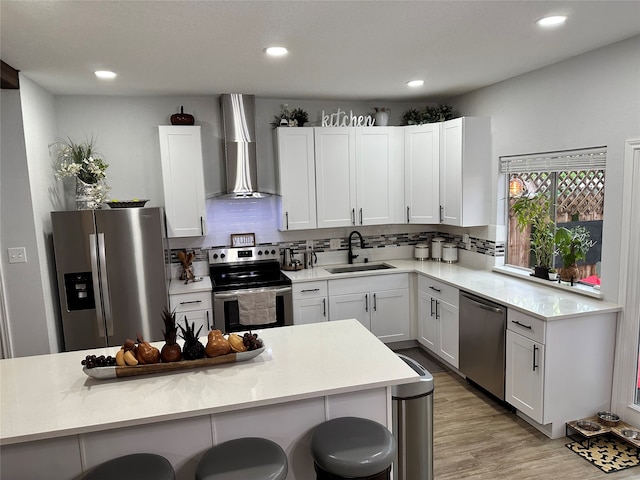 kitchen with wall chimney exhaust hood, sink, a breakfast bar area, white cabinetry, and stainless steel appliances